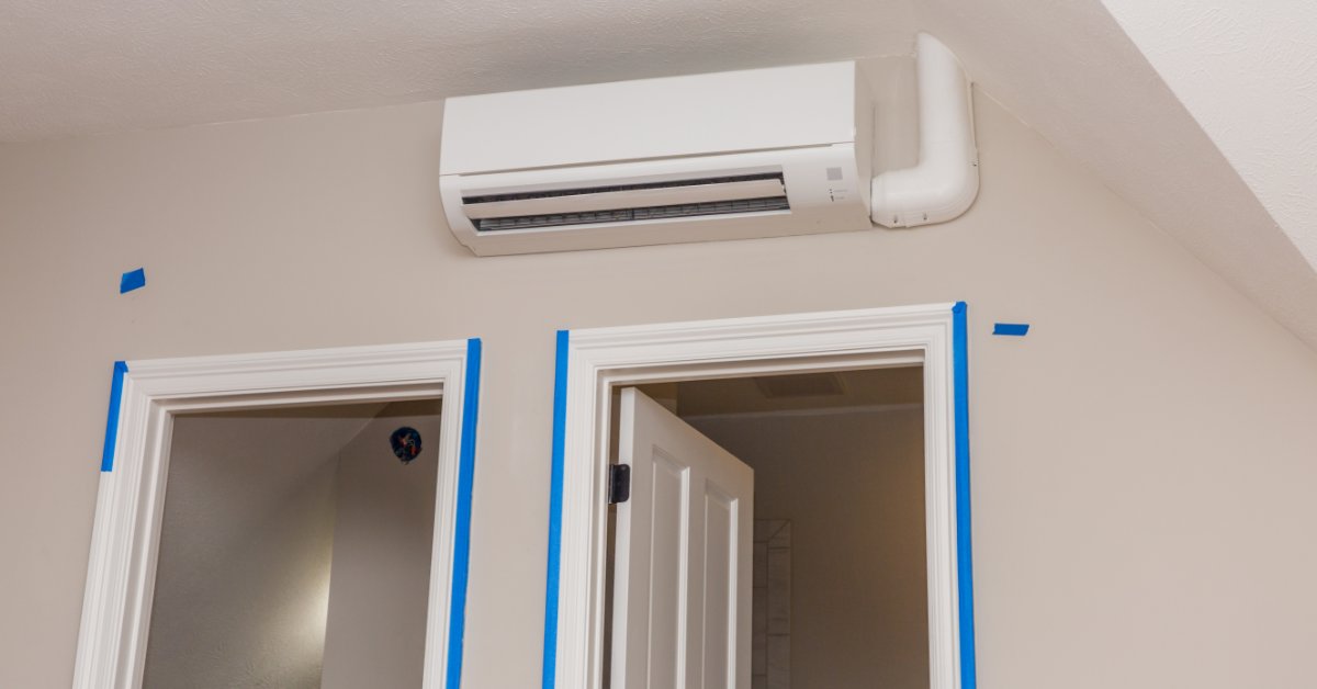 A white wall-mounted mini-split air conditioner above two doorways edged with blue painter's tape on tan walls.