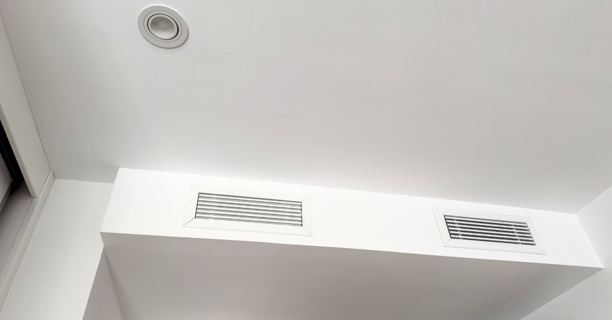 A white ceiling bulkhead with two horizontal air vents and a recessed light in a clean interior space.