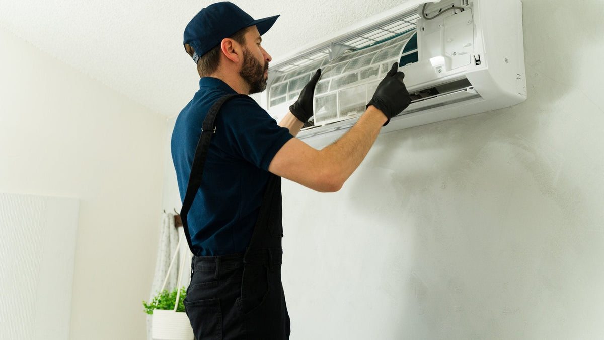 A close-up of a man removing and cleaning an air conditioner filter during maintenance of a wall-mounted indoor unit.
