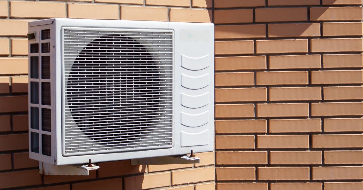 The outdoor unit of a climate-controlling air conditioning and heating system mounted on the surface of a brick wall.