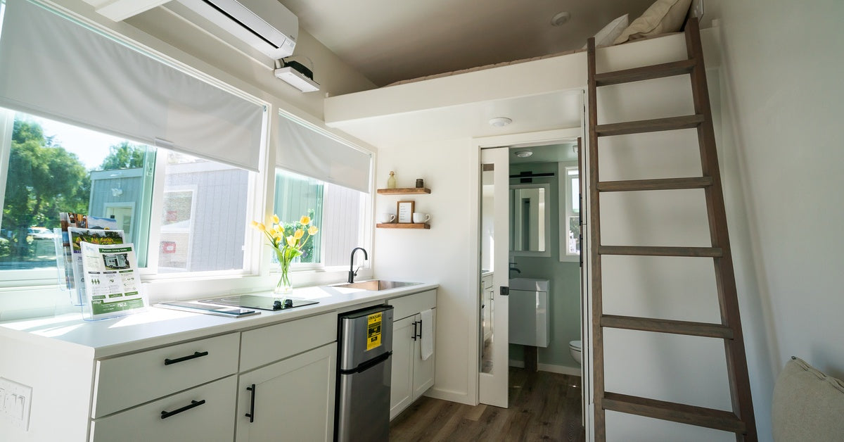 A tiny home with a mini split system mounted to the wall above the sink. The home also has a ladder leading to a loft bed in the background.