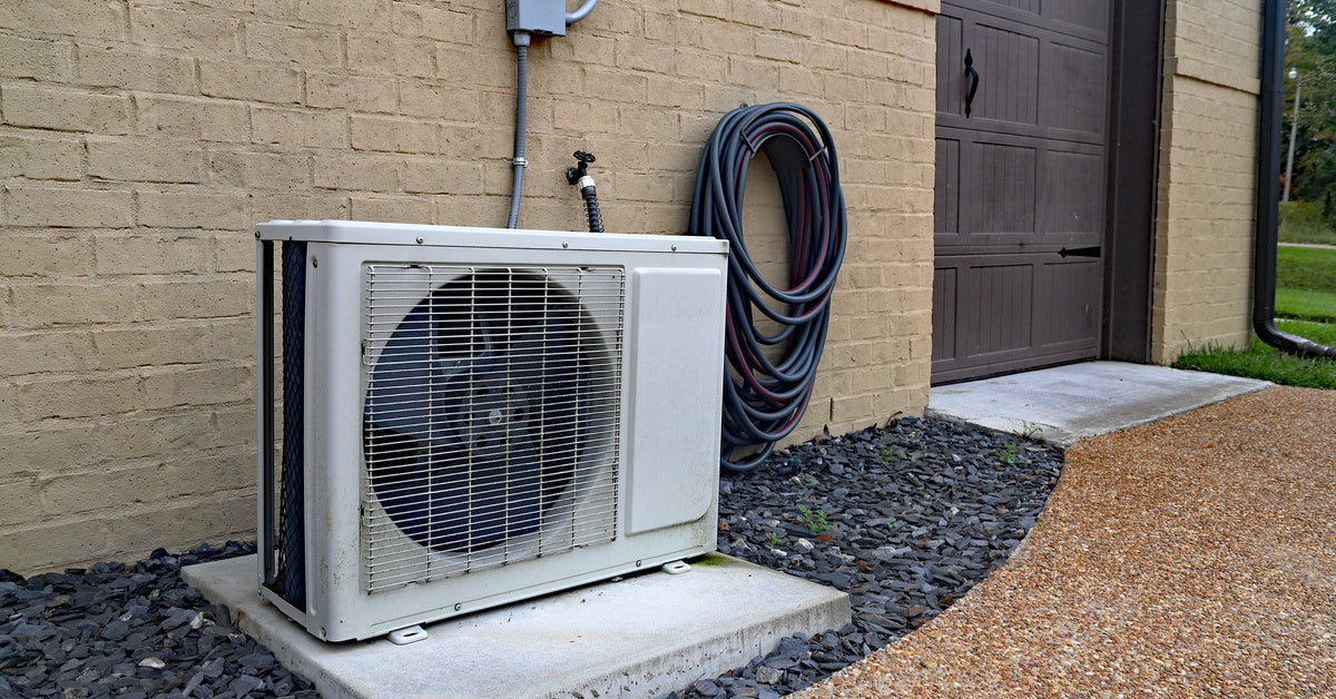 The outdoor unit of a mini-split air conditioner and heater system, against the brick wall of a property.
