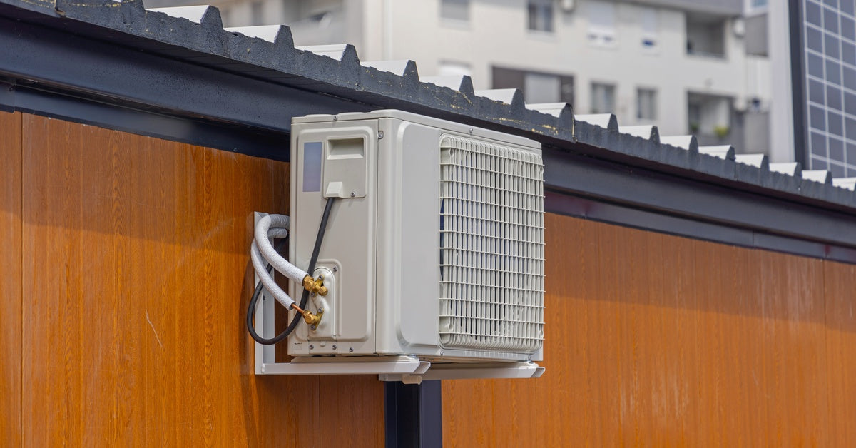The outdoor unit of a mini-split air-conditioning system mounted to a surface that is made of brown wood with black details.