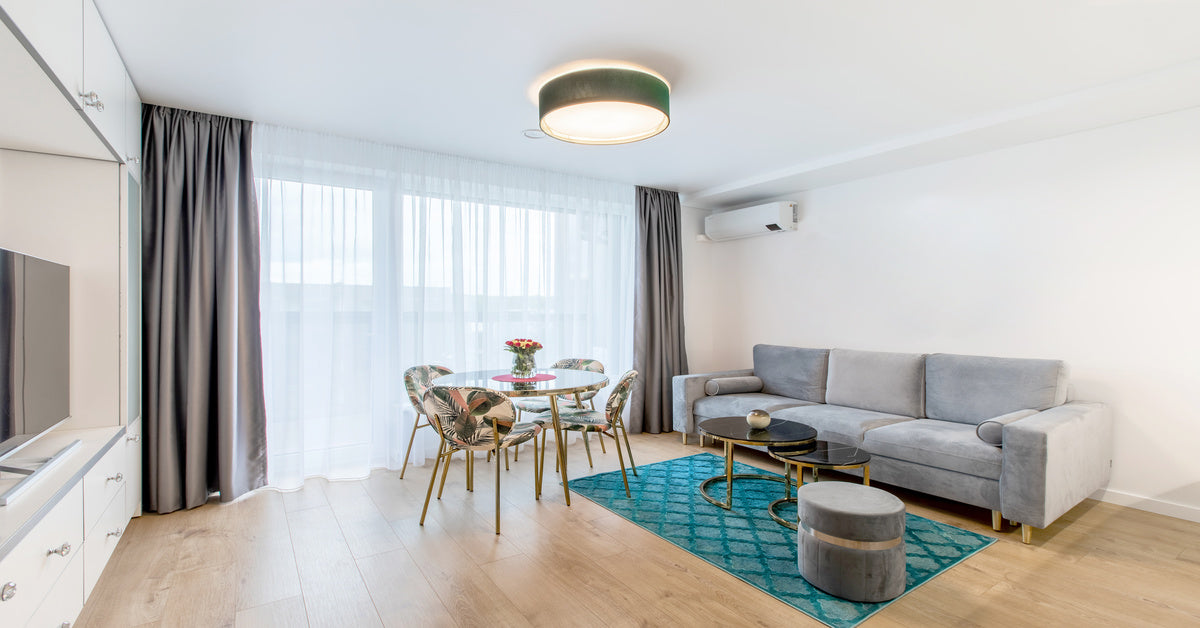 A white mini split system mounted to the surface of a white wall in an open living room with a sofa, tables, and chairs.
