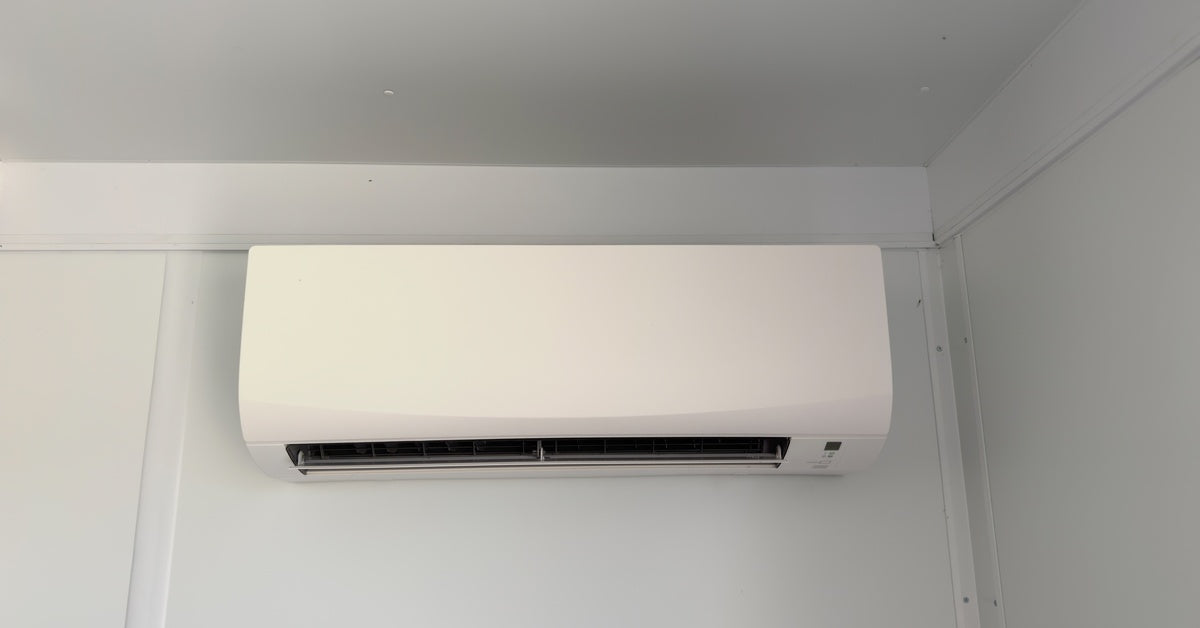 A slim, white mini split system installed high on a white wall. The mini split is inside a dimly lit room.