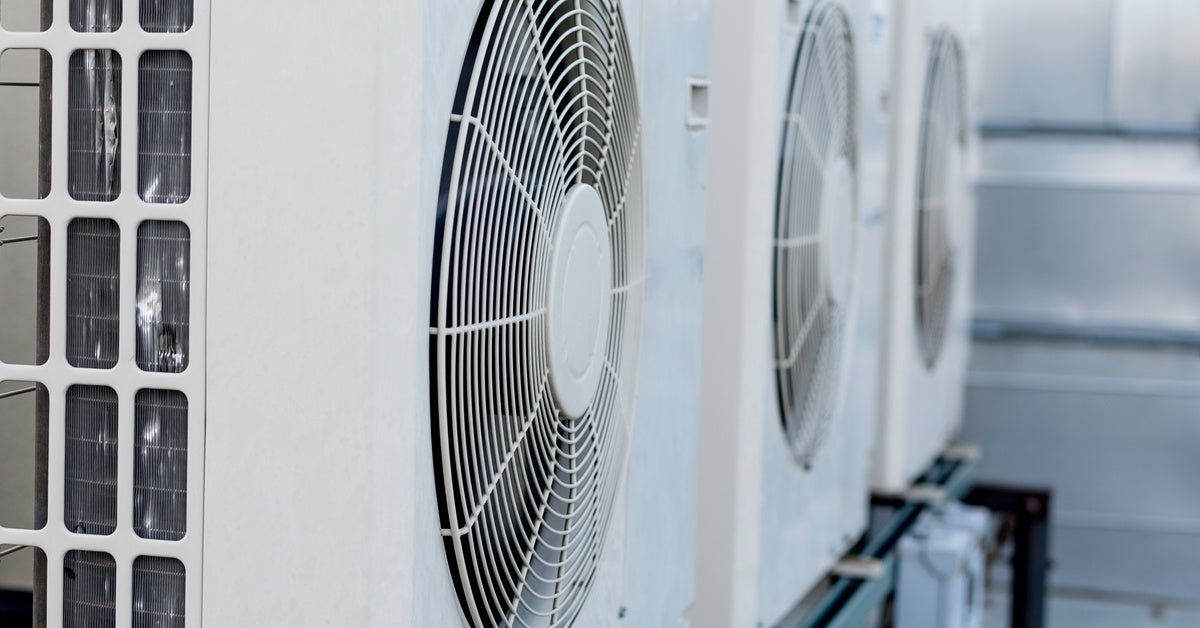 Three mini-split air conditioners hang on a white exterior wall, their fan grilles and metal piping clearly visible.
