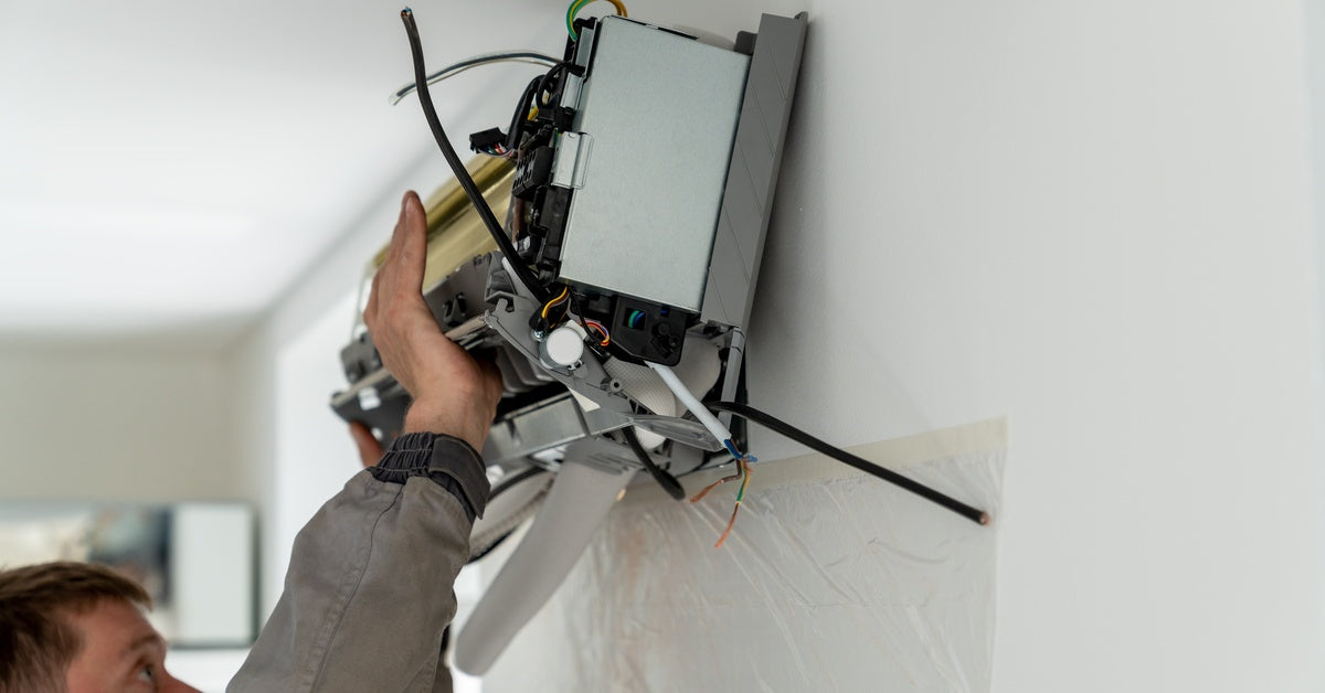 A technician installs an indoor mini-split air conditioning unit on a white wall, showing the internal components and wiring.