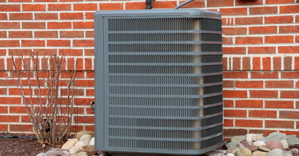 An outdoor HVAC condenser unit installed beside a brick home, sitting on a concrete pad with gravel landscaping around it.