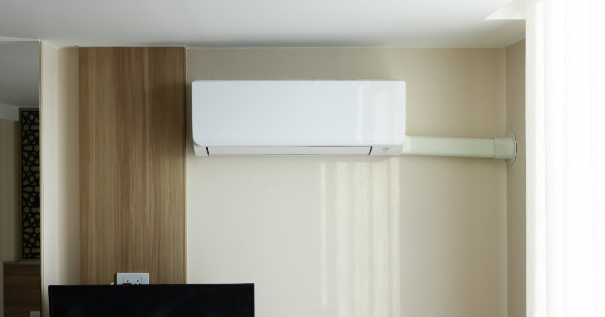 A white mini-split air handler mounted on a beige interior wall above a television in a modern living space.