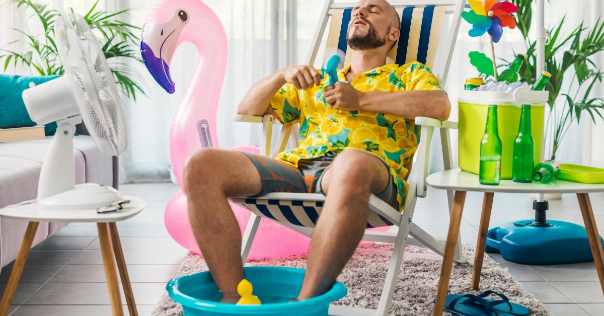 A man in a Hawaiian shirt sits in a beach chair inside his home while soaking his feet in a tub to stay cool.