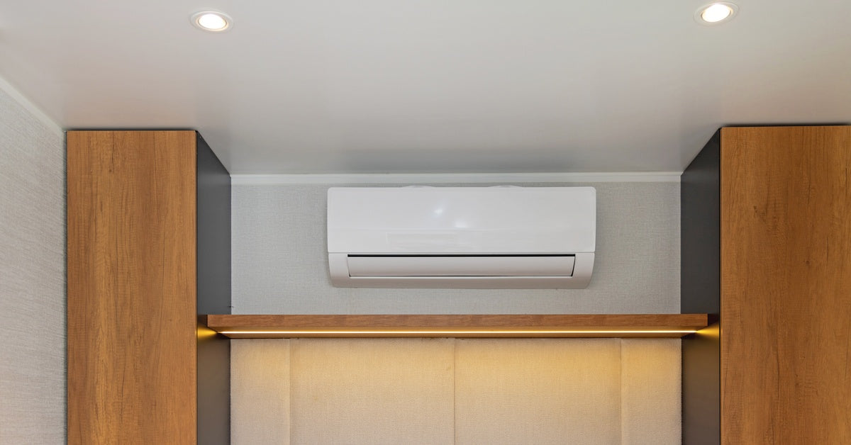 A white ductless mini-split air handler centered on a gray wall between wood cabinetry in a bedroom with recessed lighting.